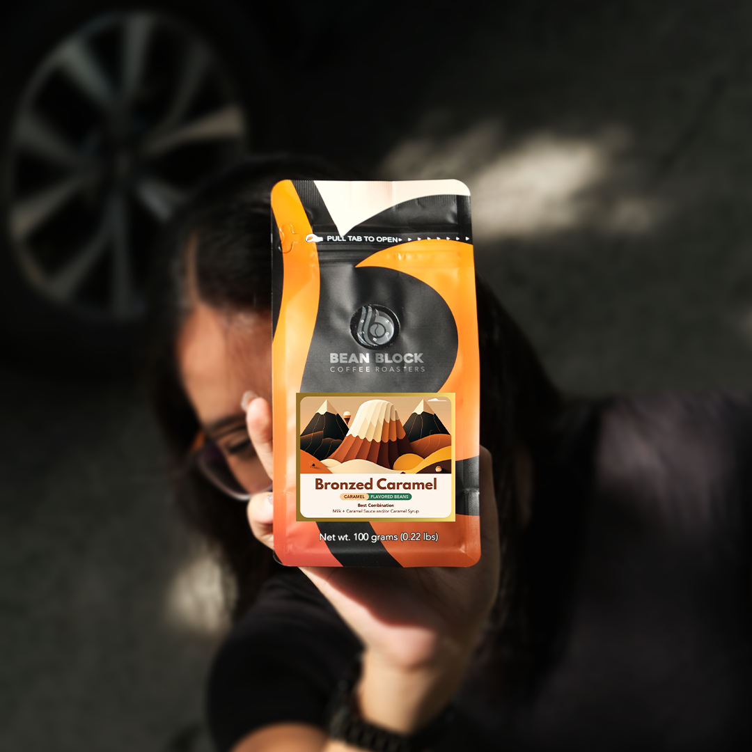 Person holding a package of Bean Block Coffee Roasters Bronzed Caramel 100g flavored coffee mix with a blurred background