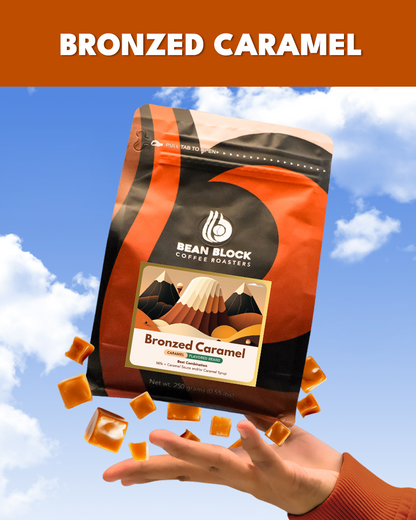 Bean Block Coffee Roasters Bronzed Caramel 250g flavored coffee bag with falling caramel pieces against a blue sky.