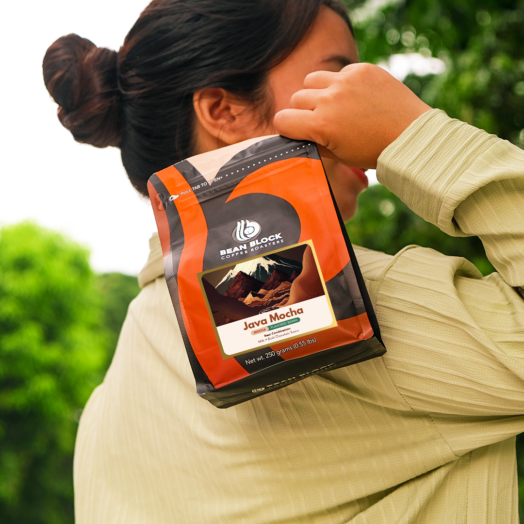 Person holding a Bean Block Coffee Roasters Java Mocha flavored 250g coffee package with a blurred green outdoor background