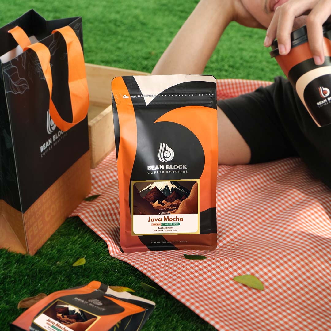 Bean Block Coffee Roasters Java Mocha 500g flavored coffee package on a checkered blanket with a person holding a coffee cup.