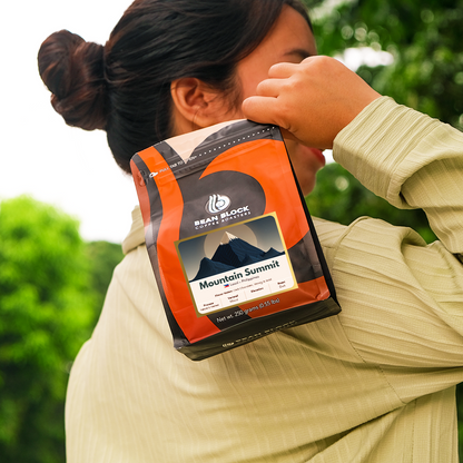 Person holding a Bean Block Mountain Summit 250g coffee package with a brand logo against a blurred green background