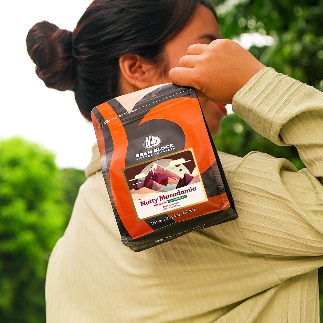 Person holding a Bean Block Coffee Roasters Nutty Macadamia 250g flavored coffee package with a blurred green background